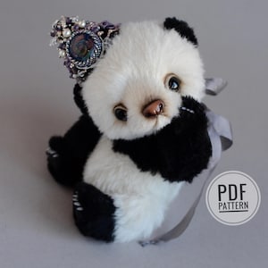 May include: A handcrafted panda bear soft toy with black and white fur, adorned with a jewelled headpiece. The panda has a light brown nose and dark eyes. A grey ribbon is tied around its neck. The image includes a "PDF PATTERN" logo.