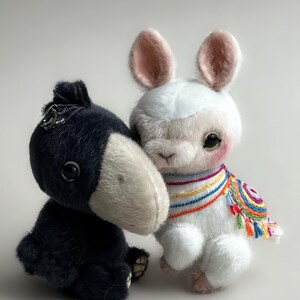 May include: Two plush toy figures: a black donkey and a white llama. The donkey has a silver accessory on its head and a light-coloured snout. The llama wears a colourful embroidered shawl with tassels.