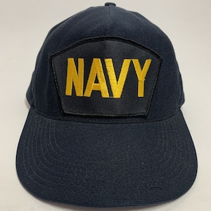 May include: A navy blue baseball cap with a black patch that says "NAVY" in gold lettering.