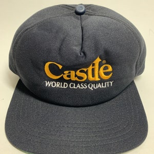 May include: A navy blue baseball cap with a yellow embroidered logo that reads "Castle World Class Quality".