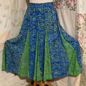 Puede incluir: Una falda estampada en azul y verde, mostrada en un maniquí. La falda tiene una tela azul con un estampado de hojas, con paneles verdes. La falda es amplia y fluida, lo que sugiere un estilo bohemio o casual.