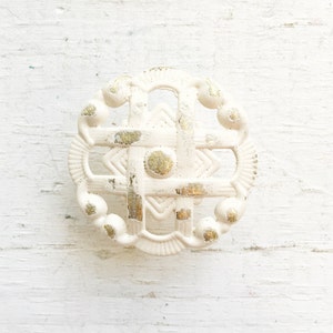 May include: White ceramic cabinet knob with a gold-painted geometric design. The knob has a circular shape and a raised edge.