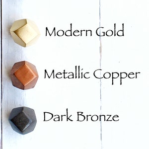 May include: Four geometric cabinet knobs in different metallic finishes: silver, gold, copper, and bronze. The knobs are arranged vertically on a white background.