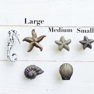 May include: A set of five decorative cabinet knobs featuring a seahorse, two starfish, a seashell, and a scallop shell. The knobs are labeled "Large", "Medium", and "Small".