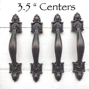 May include: Four antique-style cabinet pulls with a 3.5" center-to-center spacing. The pulls are made of metal and have a dark bronze finish.
