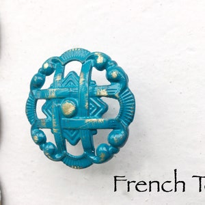 May include: Teal blue metal cabinet knob with a gold distressed finish and a geometric design. The knob is labeled "French Teal".