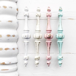 May include: Five decorative cabinet knobs with a distressed finish. The knobs are in various colors, including white, light pink, and light blue. Each knob has a unique ornate design.