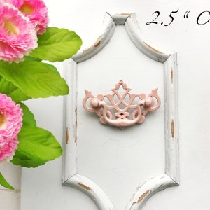 May include: A pink metal drawer pull with a decorative design. The pull is mounted on a white painted drawer front with a distressed finish. The text "2.5" Centers" is visible above the pull.