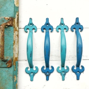 May include: Four blue and turquoise metal cabinet door pulls with a decorative fleur-de-lis design.