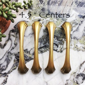 May include: Four gold cabinet pulls with a curved design. The pulls are 4.5 inches apart.
