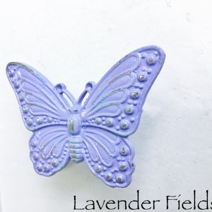 May include: A lavender butterfly-shaped cabinet knob with a distressed finish. The knob has a raised design and a silver-colored accent.