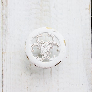May include: White round cabinet knob with a decorative floral design. The knob has a distressed white finish with hints of gold.