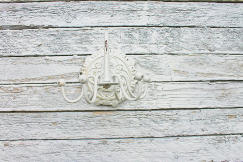 May include: White metal wall mounted coat rack with a decorative floral design and five hooks.