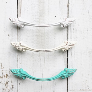 May include: Three decorative cabinet pulls with ornate details. Two are white and one is turquoise.