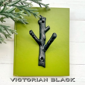 May include: A black, cast iron tree branch hook mounted on a rectangular, lime green painted wooden board. The text "VICTORIAN BLACK" is displayed at the bottom of the board. Decorative item for hanging coats, hats, or other items.