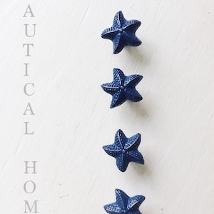May include: Four blue ceramic starfish in a vertical row on a white background. The word "NAUTICAL HOME" is written vertically on the left side of the image.