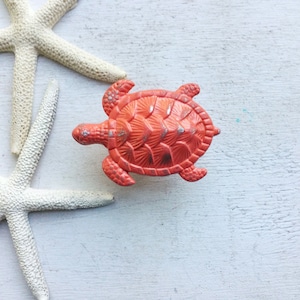 May include: Two white starfish and a bright orange ceramic turtle figurine on a white wooden background.
