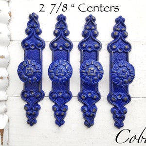 May include: Four cobalt blue cabinet knobs with ornate silver accents. The knobs are 2 7/8 inches apart.