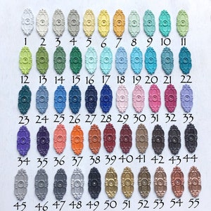 K&ouml;nnte beinhalten: Eine Tabelle mit 55 kleinen ovalen Metallteilen, die jeweils in einer anderen Farbe lackiert sind. Die Teile sind von 1 bis 55 nummeriert.