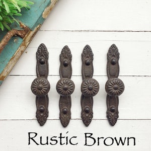May include: Four rustic brown cast iron drawer pulls with a decorative floral design. The pulls have a round knob in the center.
