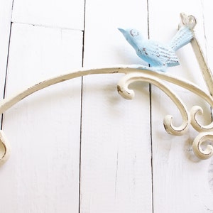 May include: White metal shelf bracket with a decorative scroll design and a blue bird figurine.
