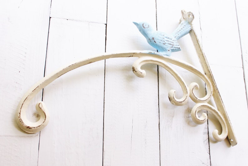 May include: White metal shelf bracket with a decorative scroll design and a blue bird figurine.