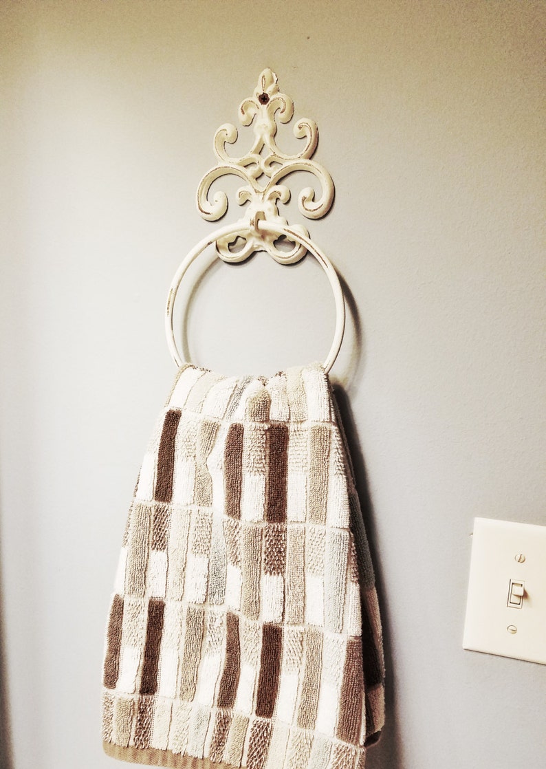 Peut inclure: Un anneau de serviette en m&eacute;tal blanc avec un motif d&eacute;coratif enroul&eacute;. Une serviette ray&eacute;e marron et blanche est accroch&eacute;e &agrave; l'anneau.