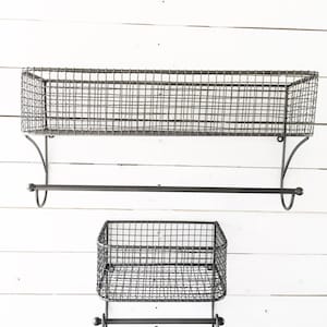 May include: Two black metal wire shelves with towel bars. The top shelf is larger and the bottom shelf is smaller. Both shelves have a simple design and are mounted on a white wall.