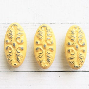 May include: Three yellow oval-shaped cabinet knobs with a decorative gray floral design.