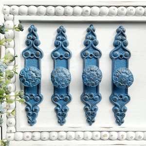 May include: Four blue metal cabinet knobs with ornate designs. Each knob has a round, raised center with a floral pattern.