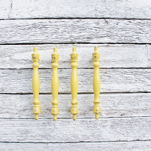 May include: Five yellow wooden drawer pulls with a decorative finial on each end. The pulls are arranged in a row against a white wood background.