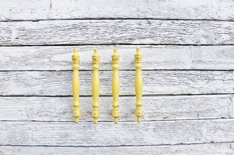 May include: Five yellow wooden drawer pulls with a decorative finial on each end. The pulls are arranged in a row against a white wood background.