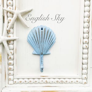 May include: White wooden sign with a blue seashell hook and two white starfish. The sign has a beaded border and the text "English Sky" is written in black.