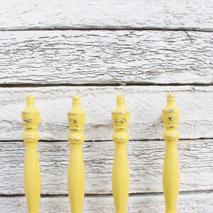 May include: Four yellow wooden finials with a distressed finish. The finials are all the same size and shape, and they are arranged in a row against a white wooden background.