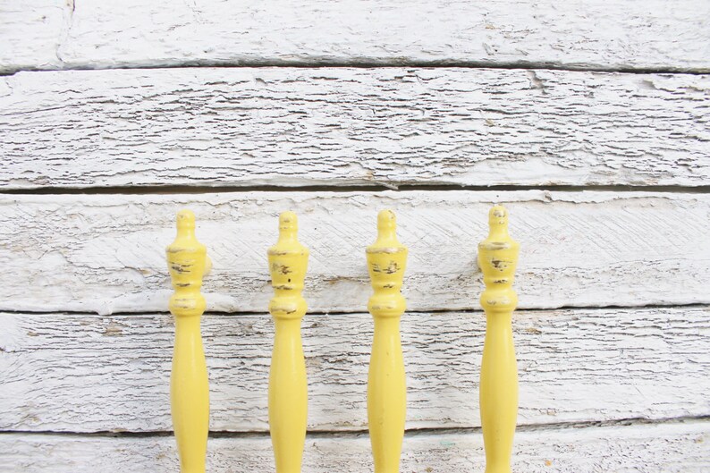 May include: Four yellow wooden finials with a distressed finish. The finials are all the same size and shape, and they are arranged in a row against a white wooden background.