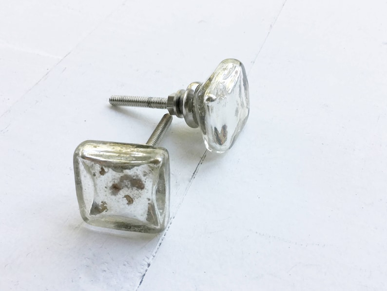 May include: Two silver square glass cabinet knobs with a distressed finish. The knobs have a silver metal screw.