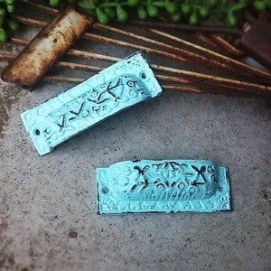 May include: Two turquoise blue metal drawer pulls with an ornate design. The pulls have a distressed finish and are perfect for adding a vintage touch to any home decor project.