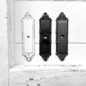 May include: Three decorative door pulls with ornate designs. One is white, one is black, and one is a dark gray.