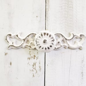 May include: White metal cabinet door pull with a decorative floral design. The pull has a round knob in the center.