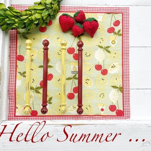 May include: A decorative display featuring a green wreath, fabric strawberries, and four vertical rods. The rods alternate between yellow and red, set against a fruit-patterned background with the text "Hello Summer ..."
