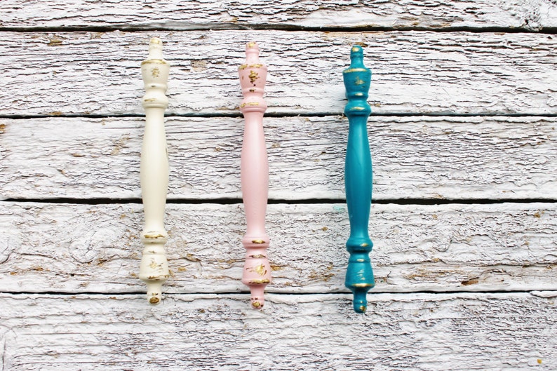 May include: Three decorative cabinet knobs with gold accents. The knobs are painted in white, pink, and teal.