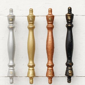 May include: Four cabinet knobs in different metallic finishes: silver, gold, copper, and black. Each knob has a decorative, ornate design.