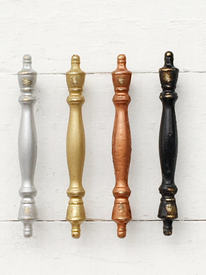 May include: Four cabinet knobs in different metallic finishes: silver, gold, copper, and black. Each knob has a decorative, ornate design.