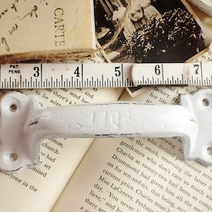 May include: White metal drawer pull with a slightly distressed finish. The pull is approximately 5 inches long and has a simple, elegant design.