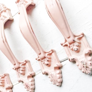 May include: Four pink metal drawer pulls with ornate designs. The pulls have a distressed finish and are perfect for adding a vintage touch to furniture.