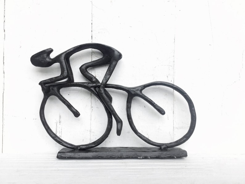 May include: Black metal sculpture of a cyclist riding a bicycle. The sculpture is on a black base.