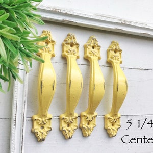May include: Four yellow metal cabinet knobs with ornate detailing. The knobs are arranged in a row and have a 5 1/4 inch center to center spacing.