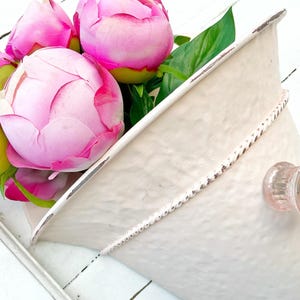 May include: A white metal cone-shaped planter with a distressed finish and a decorative knob. The planter is filled with pink peonies.