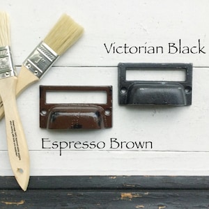 May include: Two cabinet pulls, one painted Espresso Brown and the other Victorian Black, are shown on a white surface. Two paint brushes are also shown.