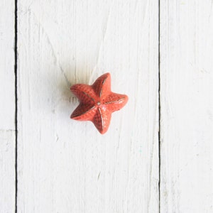 May include: A coral-colored starfish ornament on a white wooden background.